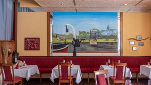 A restaurant with wooden booths, white tablecloths, and a mural of a bridge and boat.