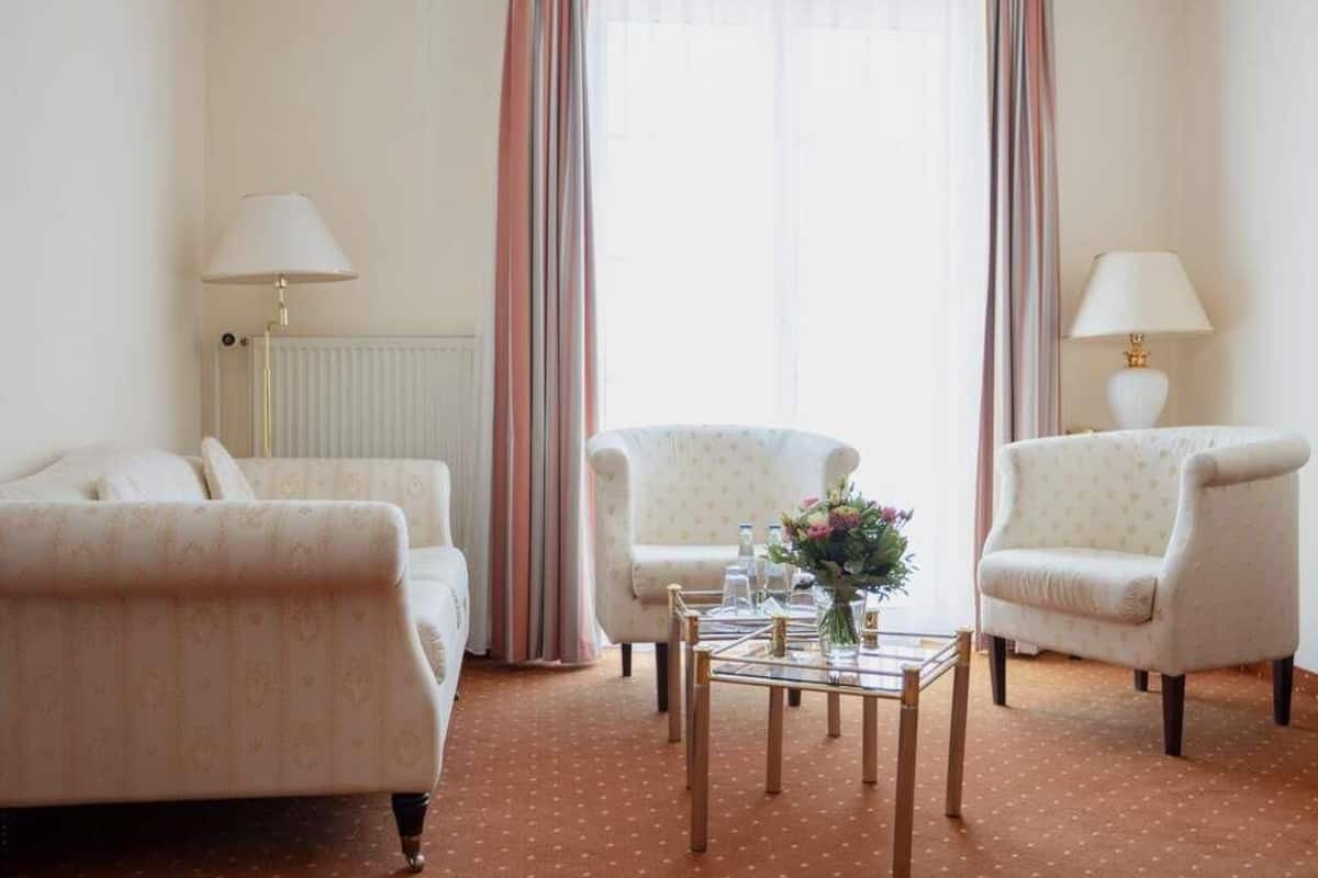 Hotellihuone, jossa on kaksi sohvaa, pieni pöytä maljakolla ja patteri.