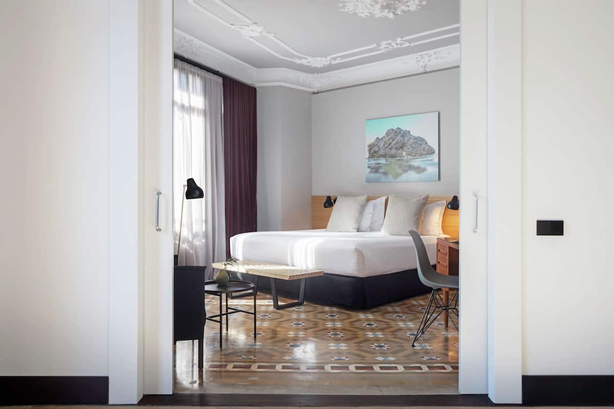 A modern hotel room with a large bed, a desk, and a chair.
