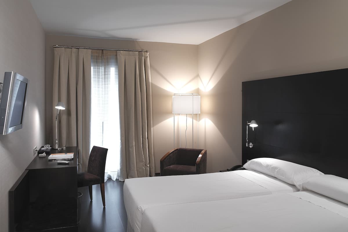 A hotel room with a bed, a desk with a chair, a TV, and a lamp.