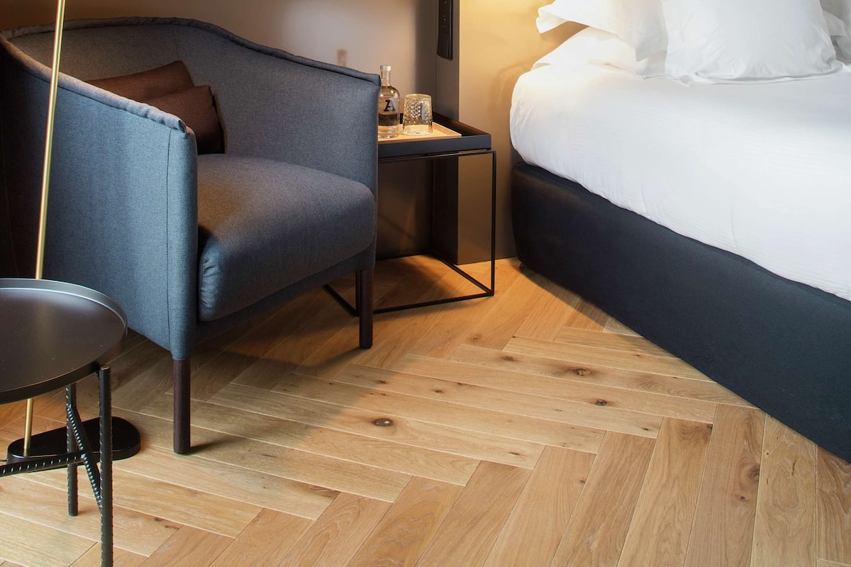 A modern hotel room with a bed, a chair, a small table, and a lamp.