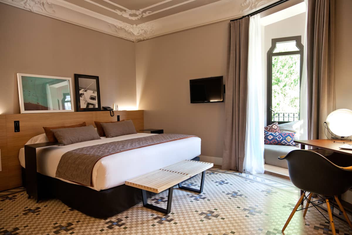 A hotel room with a large bed, a desk with a chair, a television, and a window with curtains.