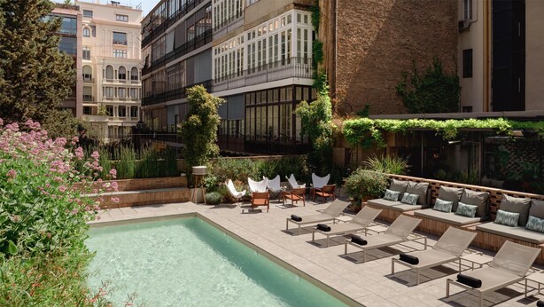 A rooftop pool area with lounge chairs and a seating area, surrounded by buildings and greenery. - Alexandra Barcelona Hotel, Curio Collection by Hilton (Barcelona)
