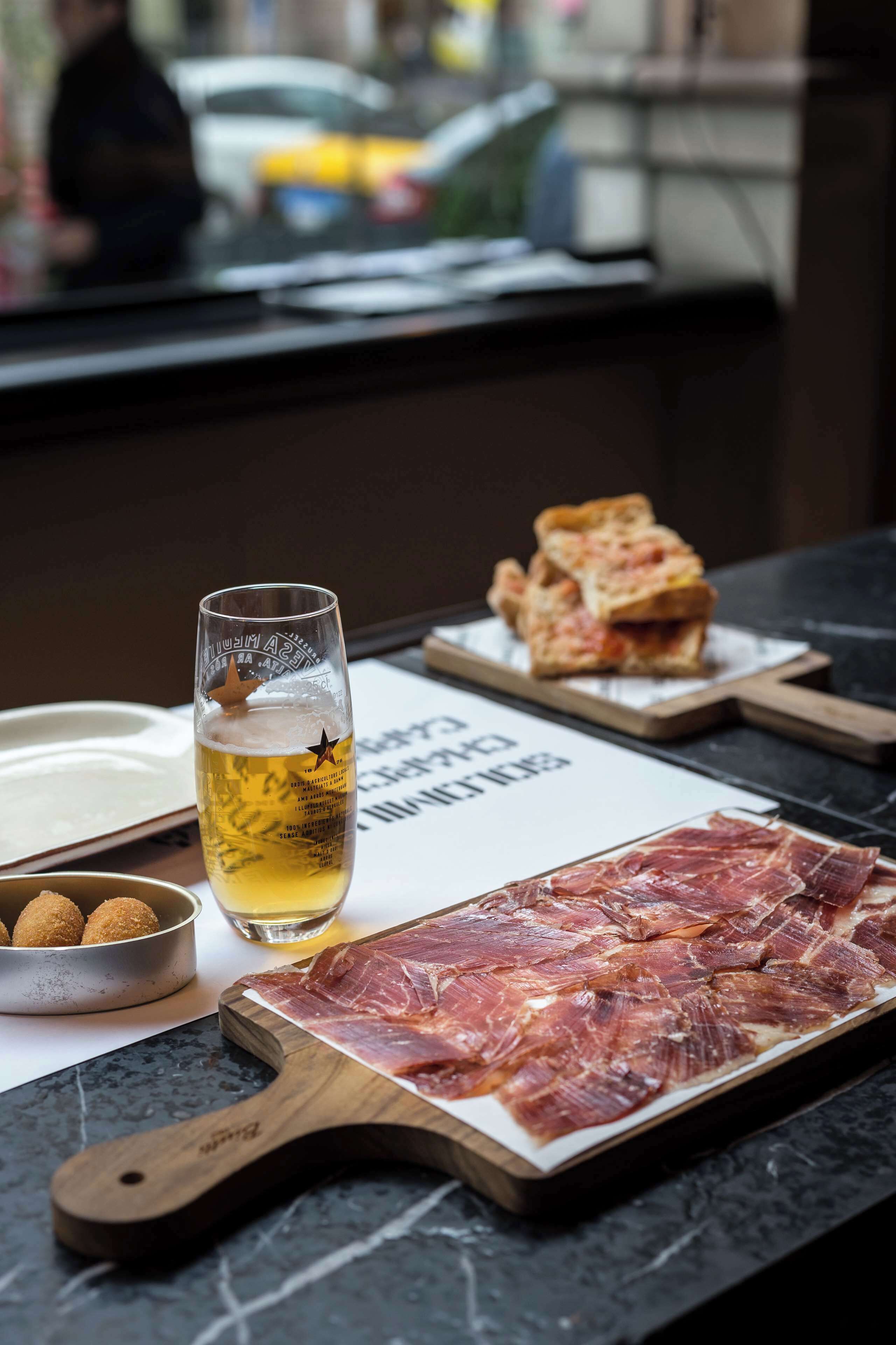 Une table avec un verre de bière, une assiette de jambon cru et un bol de croquettes.