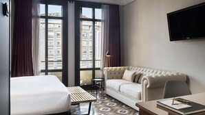 A hotel room with a bed, a sofa, a desk, and a TV. - Alexandra Barcelona Hotel, Curio Collection by Hilton (Barcelona)