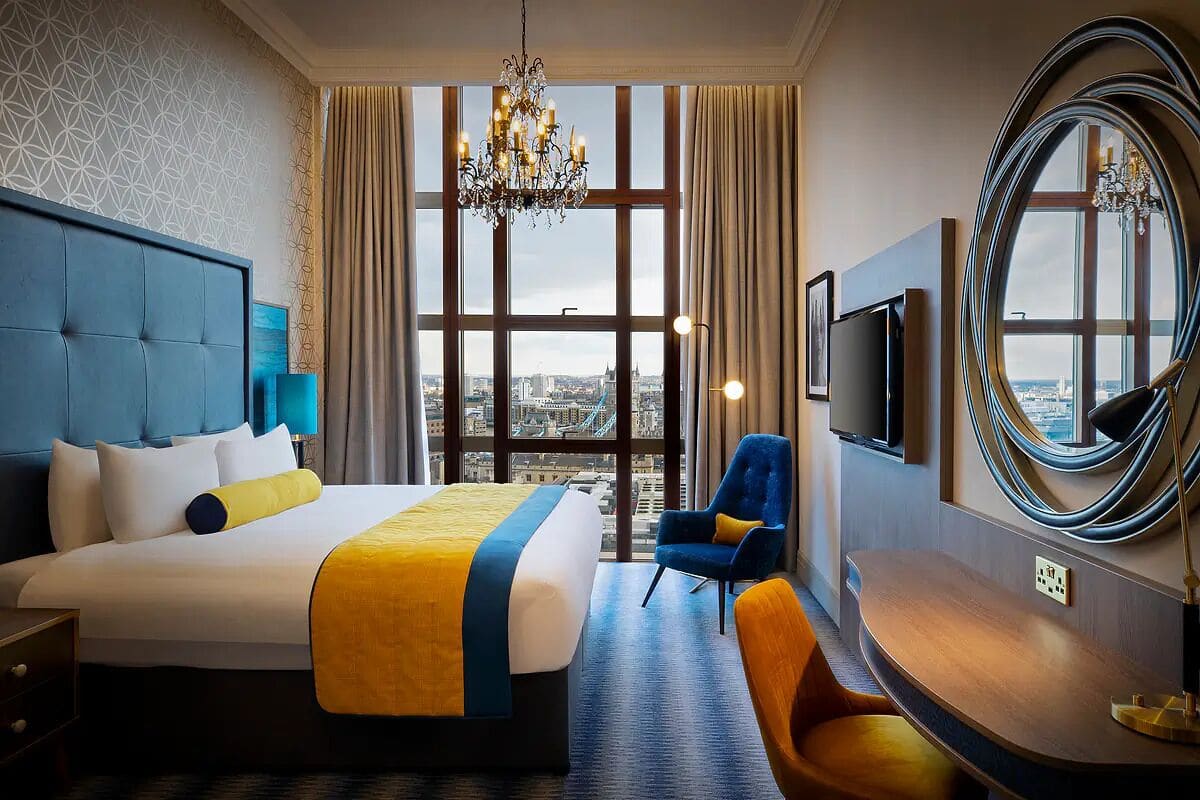 Une chambre d’hôtel avec un grand lit, un bureau, une chaise, une télévision et une vue sur la ville grâce à de grandes fenêtres.