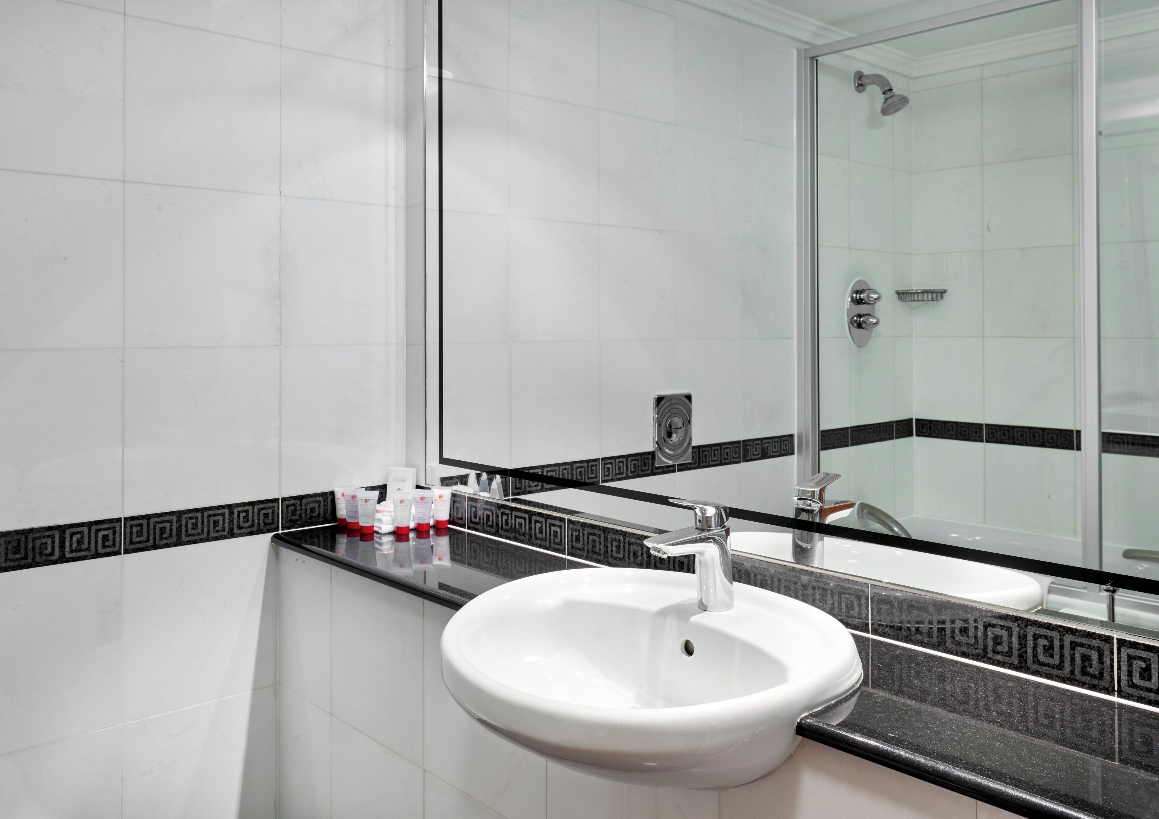 Une salle de bain avec un lavabo blanc, une cabine de douche en verre et un miroir.