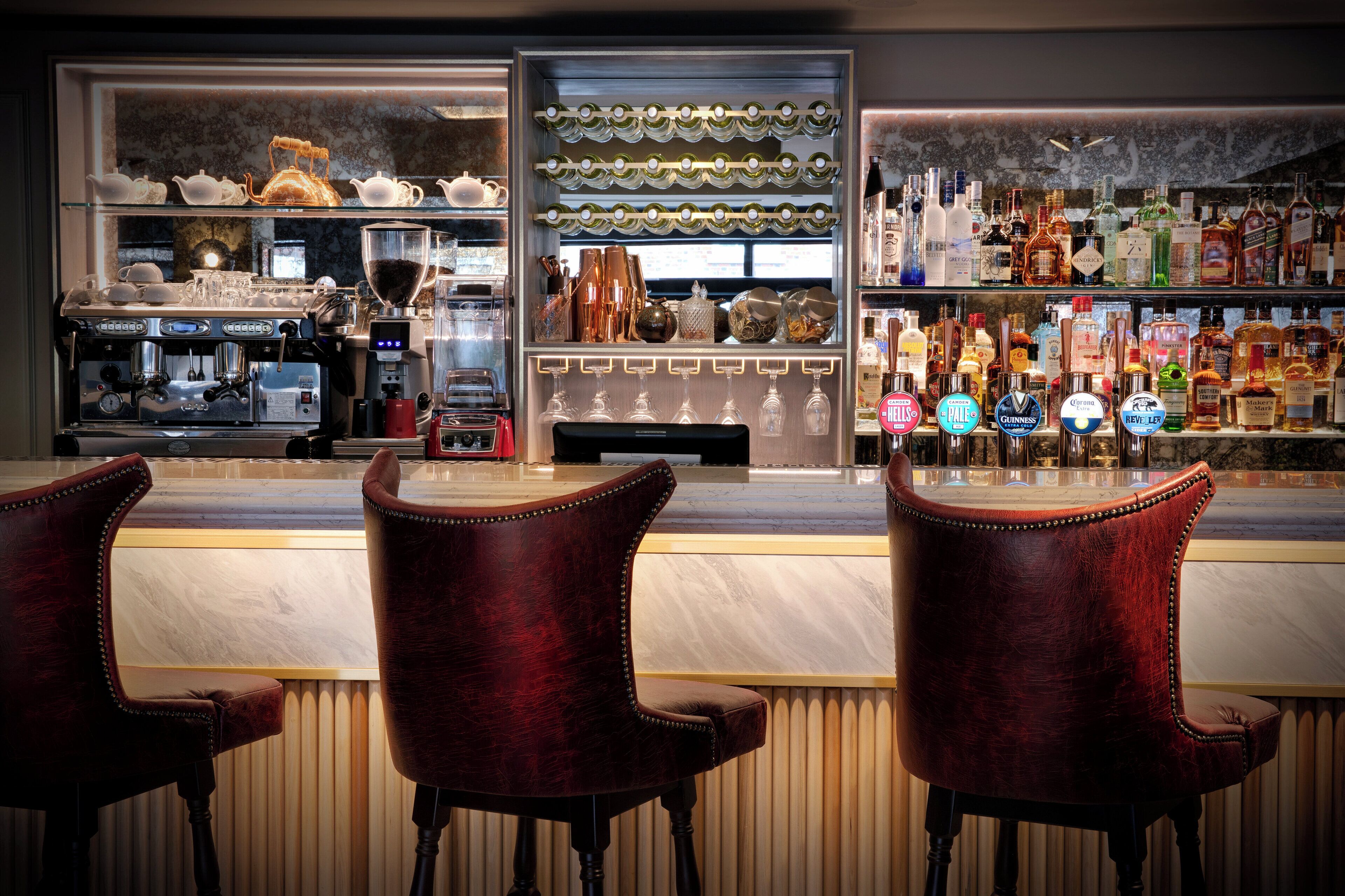 A bar area with a coffee machine, wine glasses, and a variety of liquor bottles.