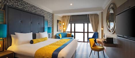 A hotel room with a large bed, a desk, a chair, and a TV.