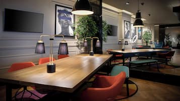A modern dining area with a long wooden table, multiple chairs, pendant lighting, and framed artwork on the walls.