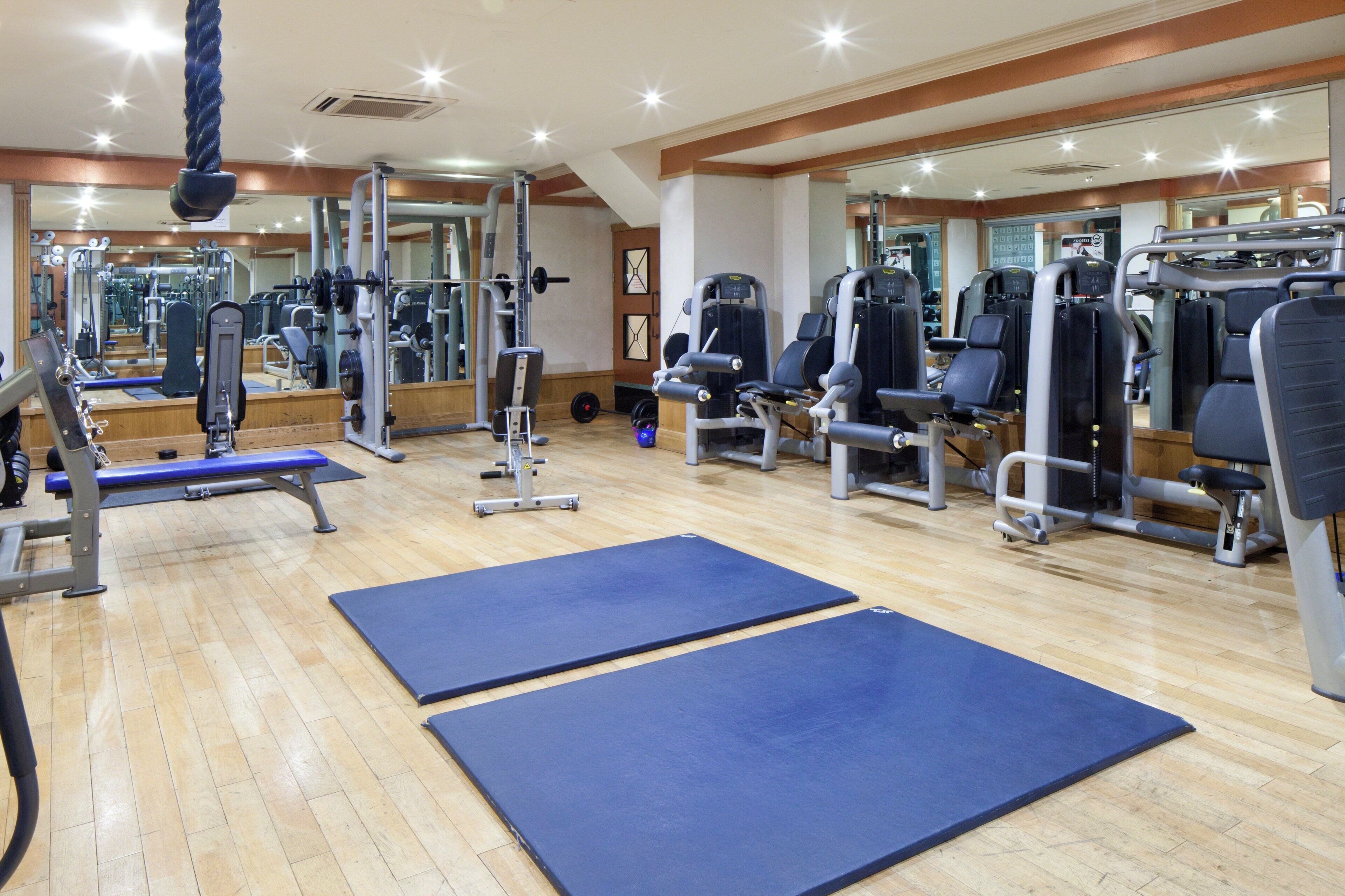 A gym with various exercise equipment, wooden floors, and blue mats.