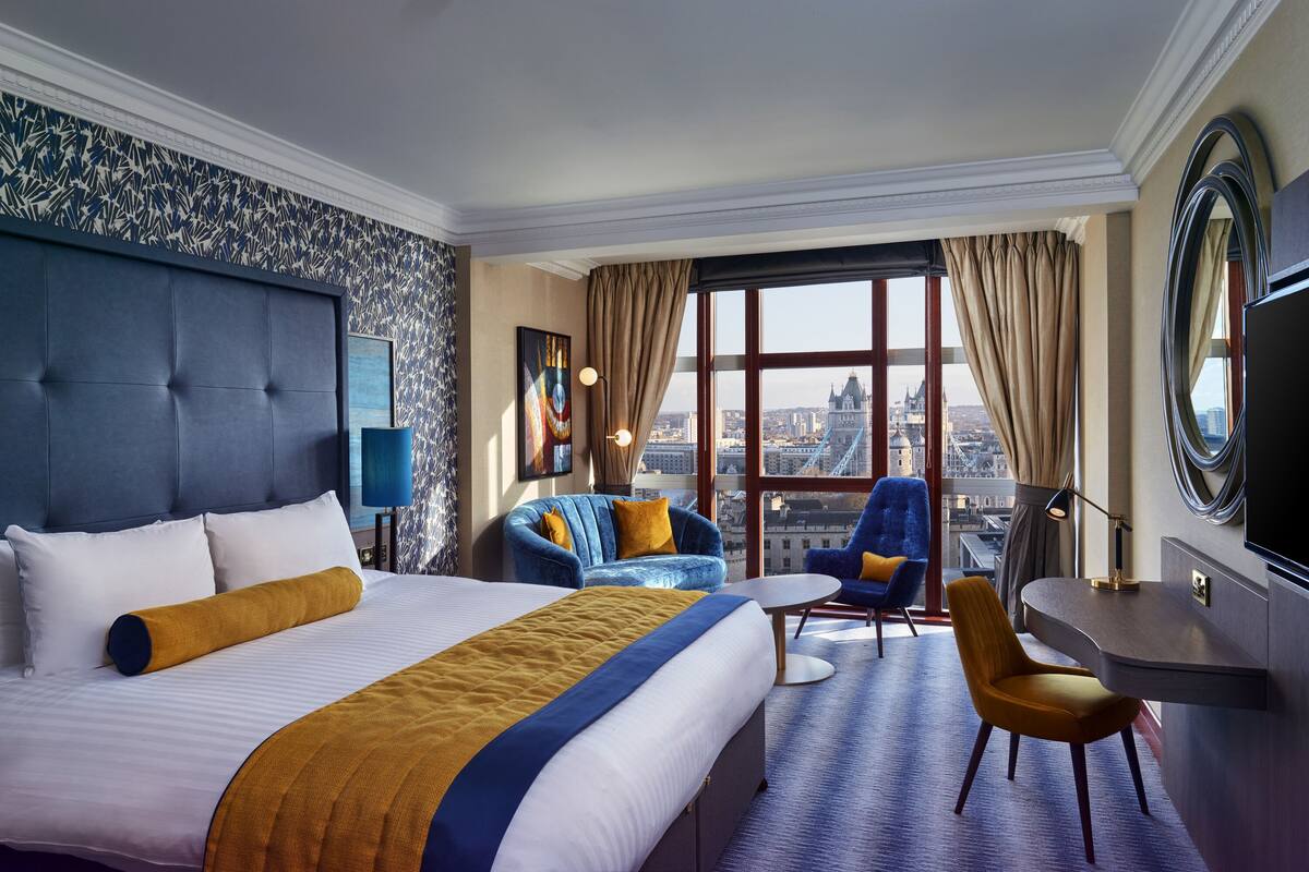 Une chambre d’hôtel avec un grand lit, deux fauteuils, un bureau et une vue sur la ville.
