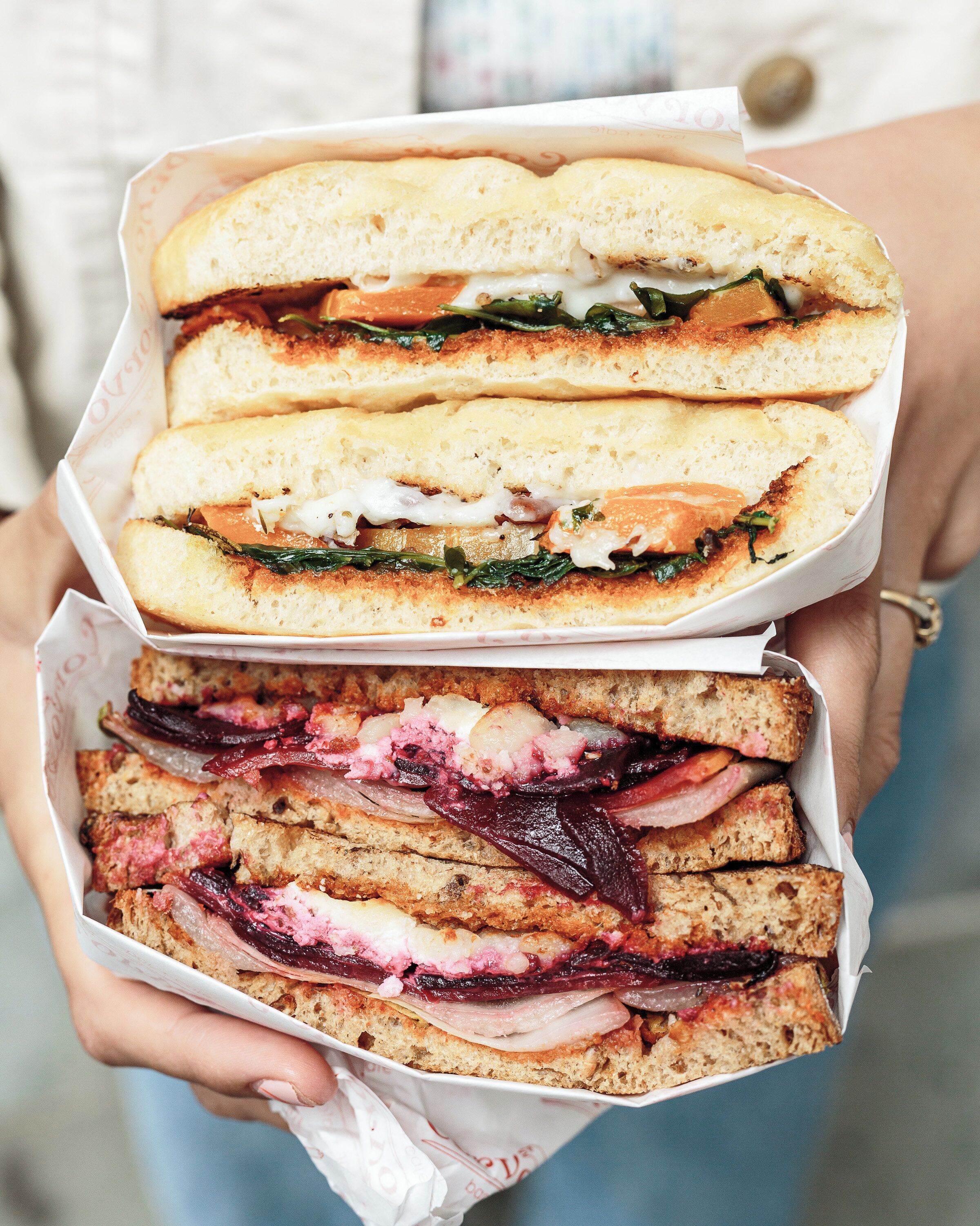Une personne tenant deux sandwichs dont on peut voir la garniture.