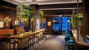 A bar area with wooden bar counters, stools, and a view of the street outside. - Leonardo Royal Hotel London City - Tower of London (London)