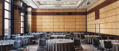 A large conference room with multiple round tables and chairs, a projector, and a large window on the left side.