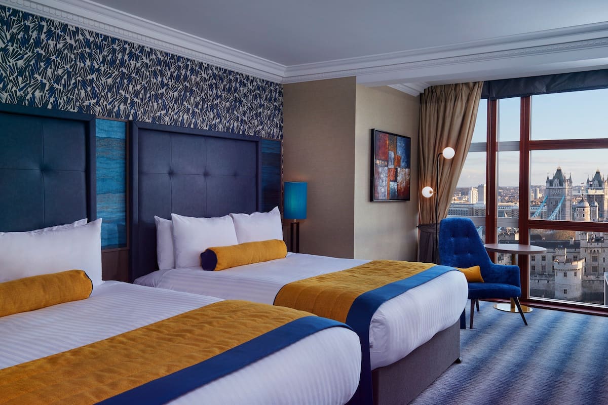 A hotel room with two beds, a view of the city, and a blue chair.