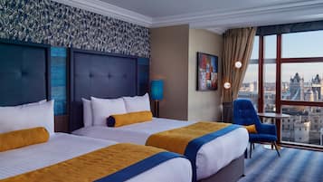 Ein Hotelzimmer mit zwei Betten, Blick auf die Stadt und einem blauen Sessel.
