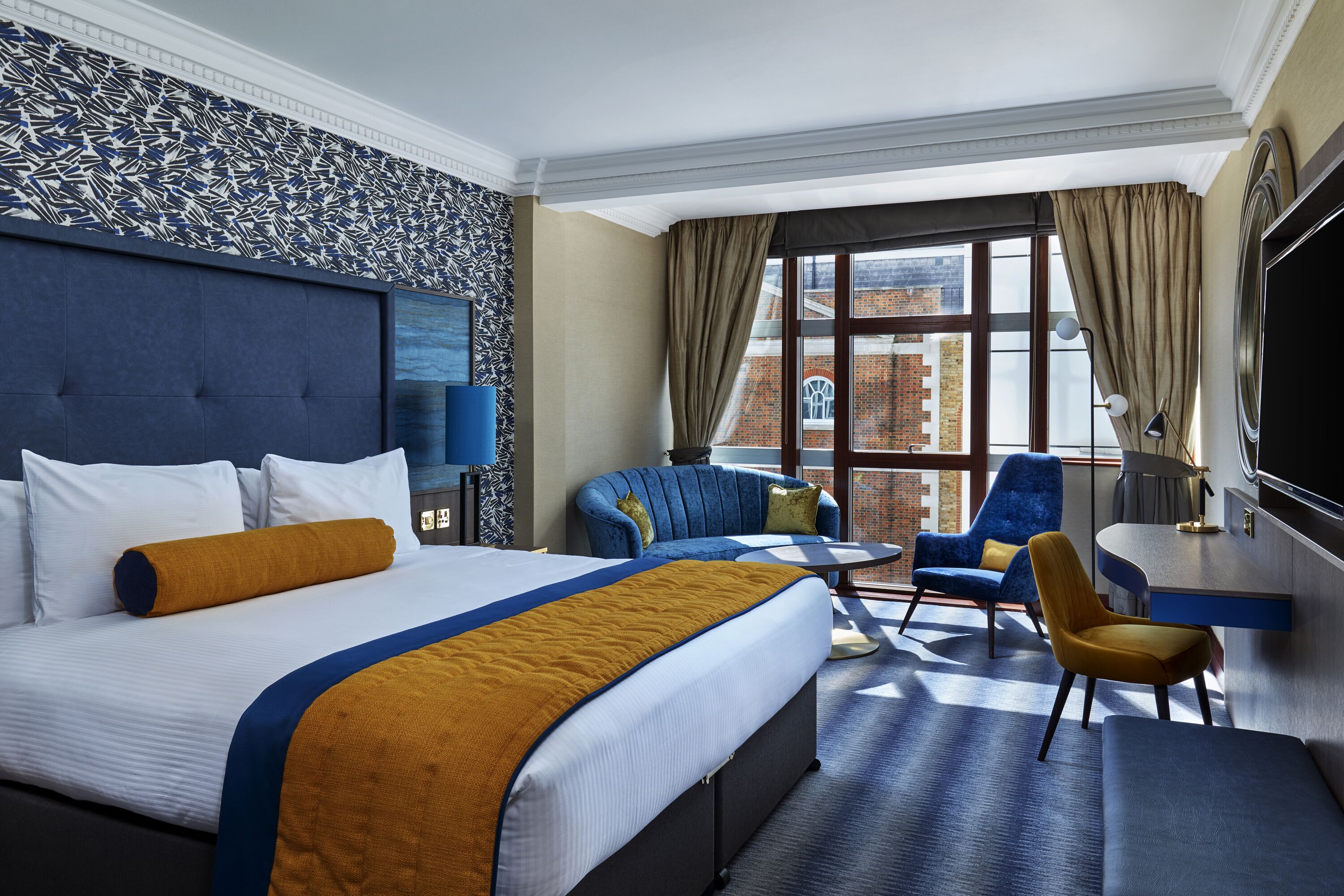 A hotel room with a large bed, a sofa, a desk, and a TV.
