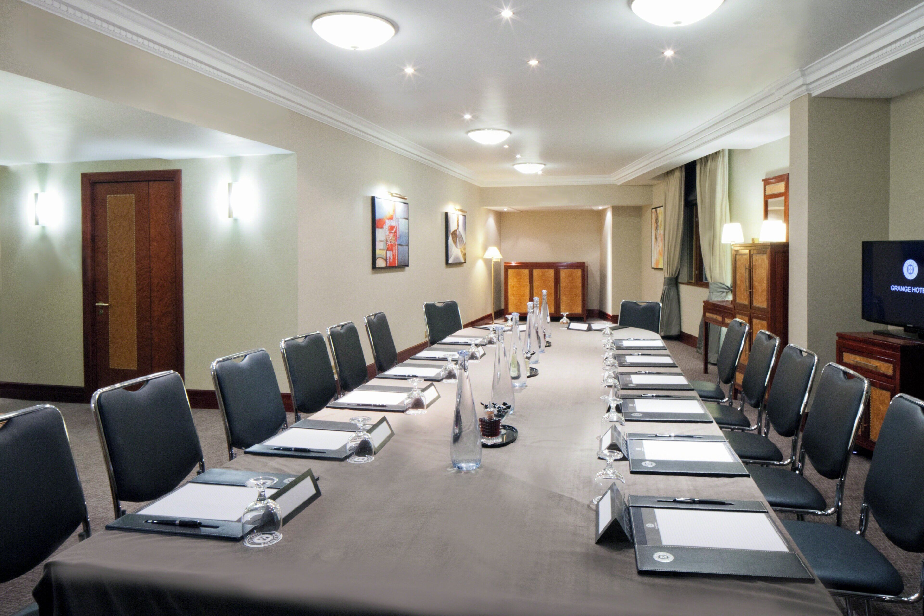 A conference room with a long table, chairs, nameplates, and a television.