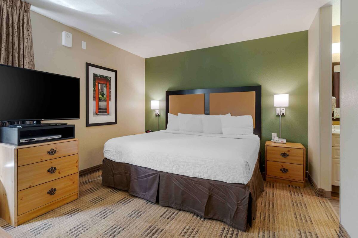 Una habitació d'hotel amb un llit gran, una televisió sobre una petita taula de nit de fusta i dues làmpades de nit.