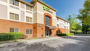A Stay America hotel with a lobby entrance, a parking lot, and a clear sky.