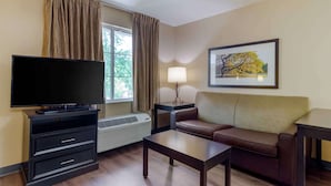 A living room with a flat-screen TV, a sofa, a coffee table, a lamp, and a window with curtains.