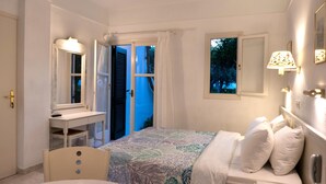 A bedroom with a bed, bedside table, and a window with a view of trees. - Villea Village by GHH (Sitia)