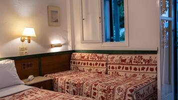 A room with two beds, a bedside table with a lamp, a phone, and a window with a view of greenery.