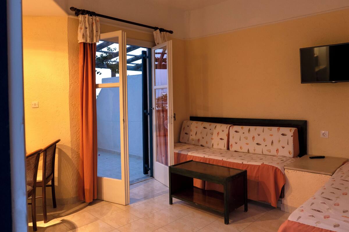 A room with a bed, a small table, a sofa, and a TV mounted on the wall.