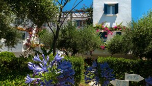 A building with a white facade, blue shutters, and a balcony with pink flowers. There are directional signs with numbers 501-510, 601-606, and 701-703. - Villea Village by GHH (Sitia)