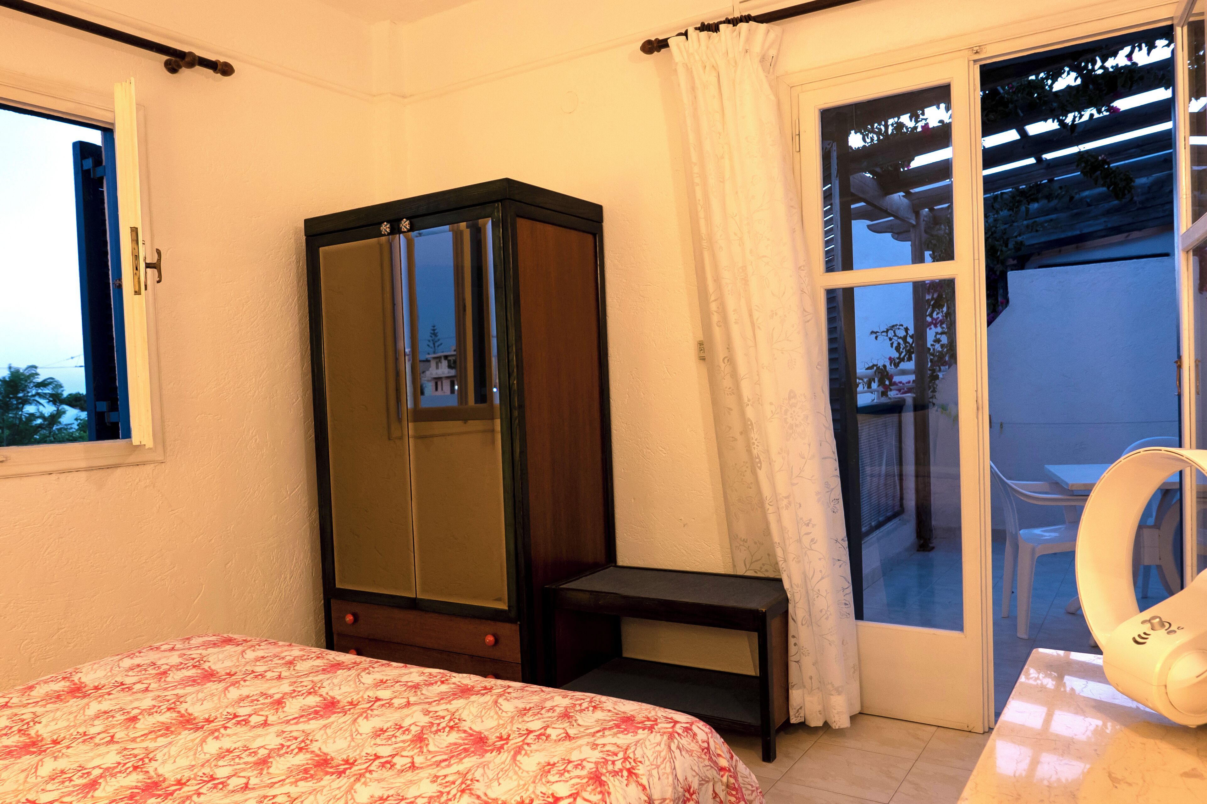 Ein Schlafzimmer mit Bett, Kleiderschrank, einem kleinen Tisch und einer Glastür zu einem Außenbereich.