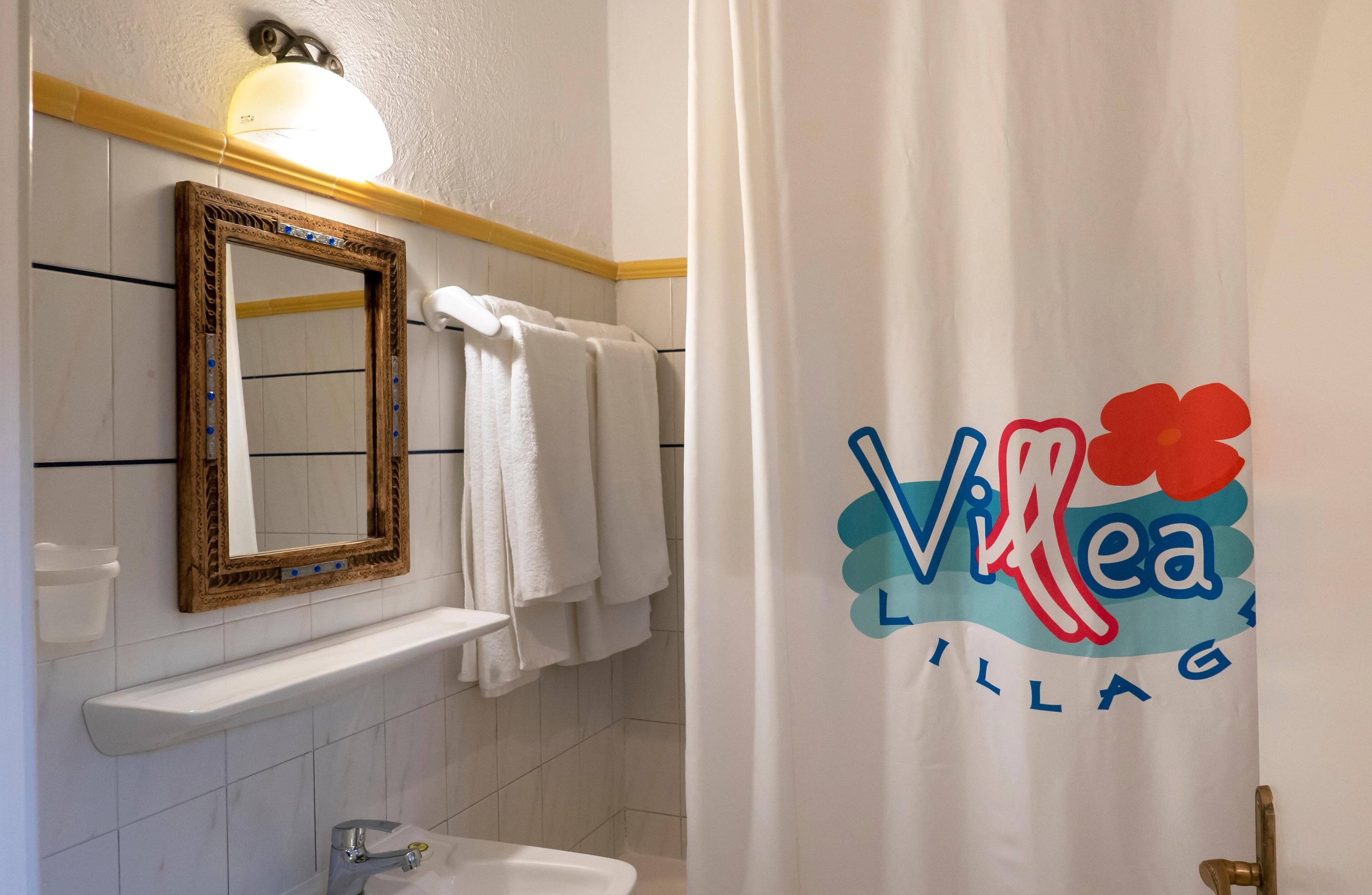 A bathroom with a mirror, towel rack, sink, and a shower curtain with a logo.