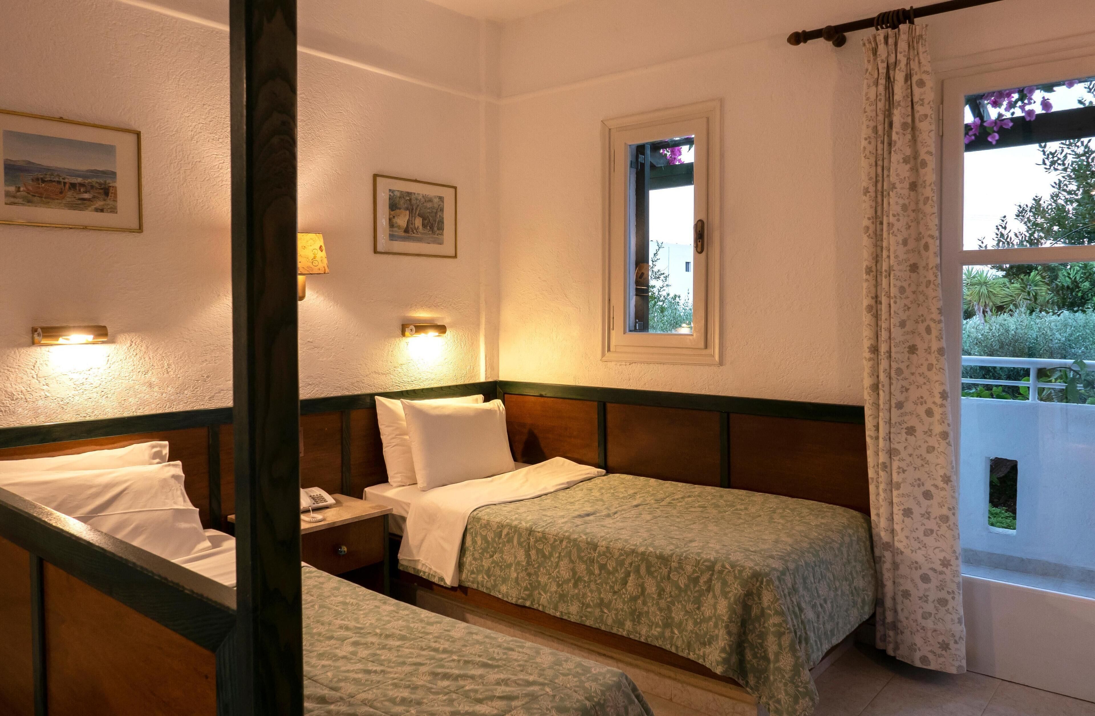 Une chambre avec deux lits, une table de chevet, une lampe de chevet, une fenêtre donnant sur un paysage verdoyant et une porte avec un rideau.