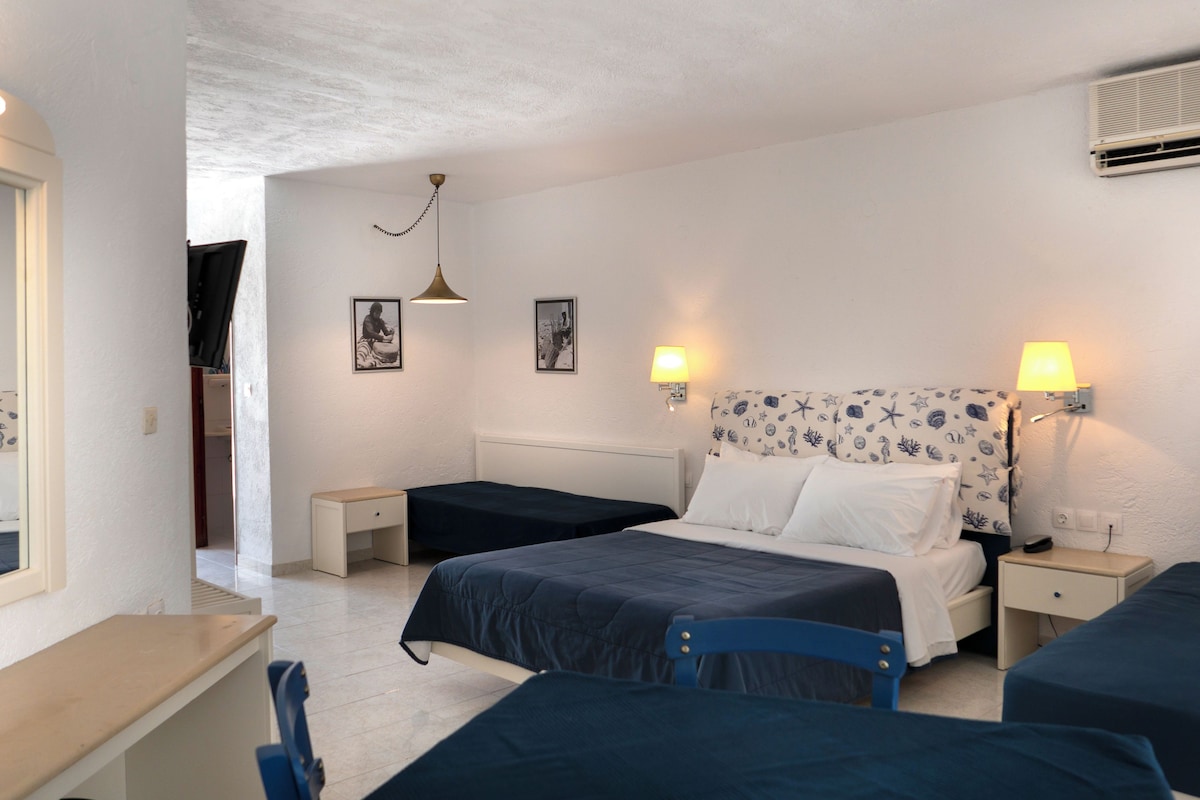A bedroom with two single beds, a desk, and a chair. There are two bedside tables with lamps, a ceiling fan, and framed pictures on the wall.