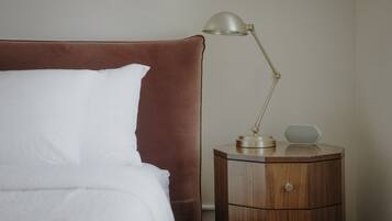 A bed with a brown headboard and a white pillow, a bedside table with a lamp, and a small speaker.