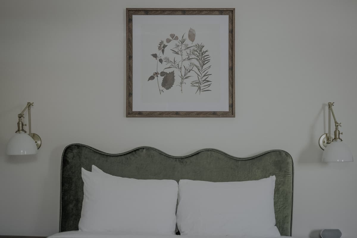 Un lit avec une tête de lit verte, des oreillers blancs et deux lampes fixées au mur.