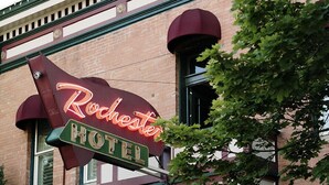 Un bâtiment en briques sur lequel est apposée une enseigne au néon indiquant « Rochester Hotel ».