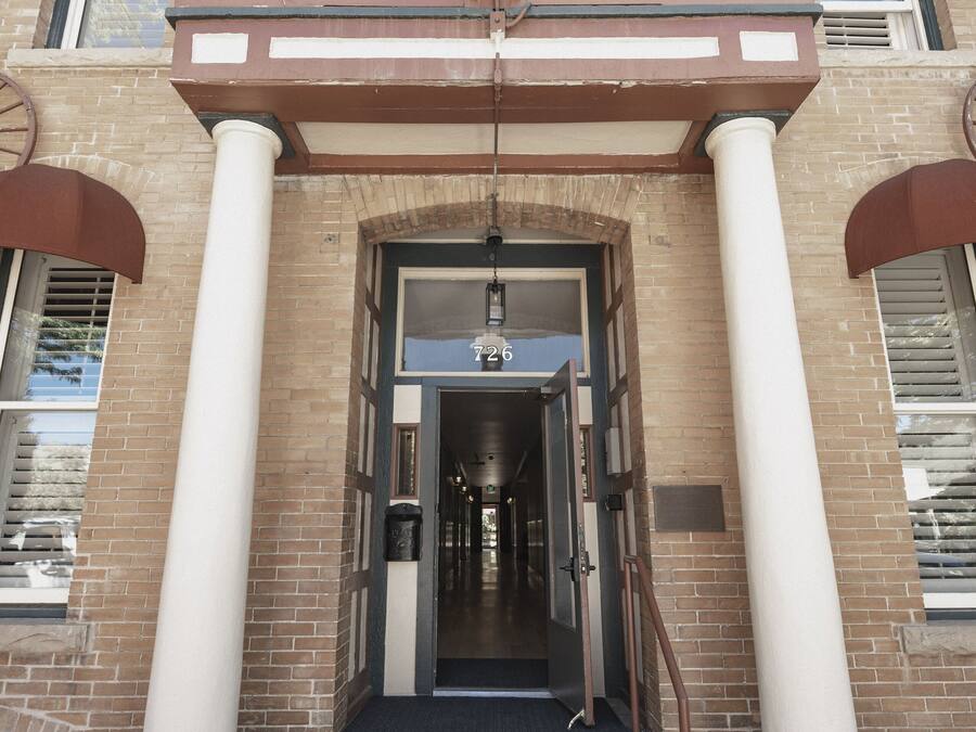Fachada de edificio de ladrillo con altas columnas blancas y un toldo metálico.