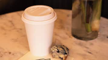 A white disposable cup with a lid, a small piece of bread, and a note with the word "peeps" on a marble table.