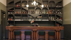 Un espace bar avec de nombreuses étagères remplies de bouteilles d’alcool et de verres, un comptoir en bois et trois tabourets de bar.