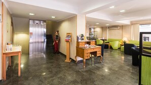 A lobby with a reception desk, a coffee machine, a vending machine, a staircase, and a seating area with green sofas. - Botanico Hotel (Lisbon)