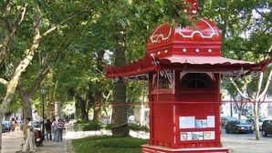 A red pavilion with a domed roof, surrounded by a chain-link fence, and located in a park with trees and a paved walkway. - Botanico Hotel (Lisbon)