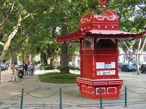 A red pavilion with a domed roof, surrounded by a chain-link fence, and located in a park with trees and a paved walkway.