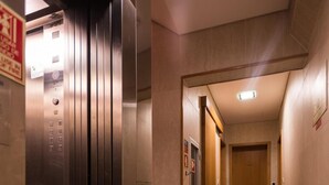 A modern elevator with a control panel, a tiled corridor, and a wooden door at the end.