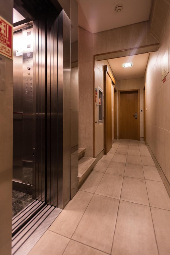 A modern elevator with a control panel, a tiled corridor, and a wooden door at the end. - Botanico Hotel (Lisbon)