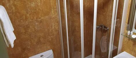 A bathroom with a glass-enclosed shower, a toilet, and a sink.