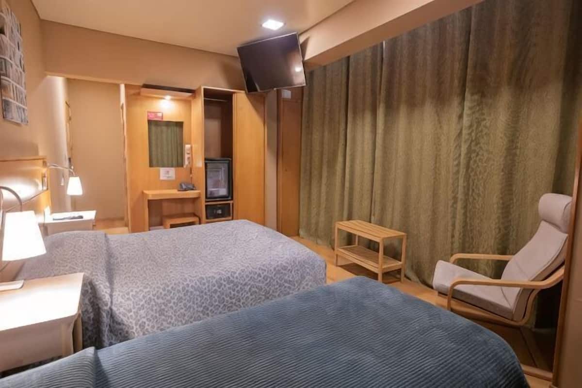 A hotel room with two beds, a TV, a desk, a chair, and a curtain.