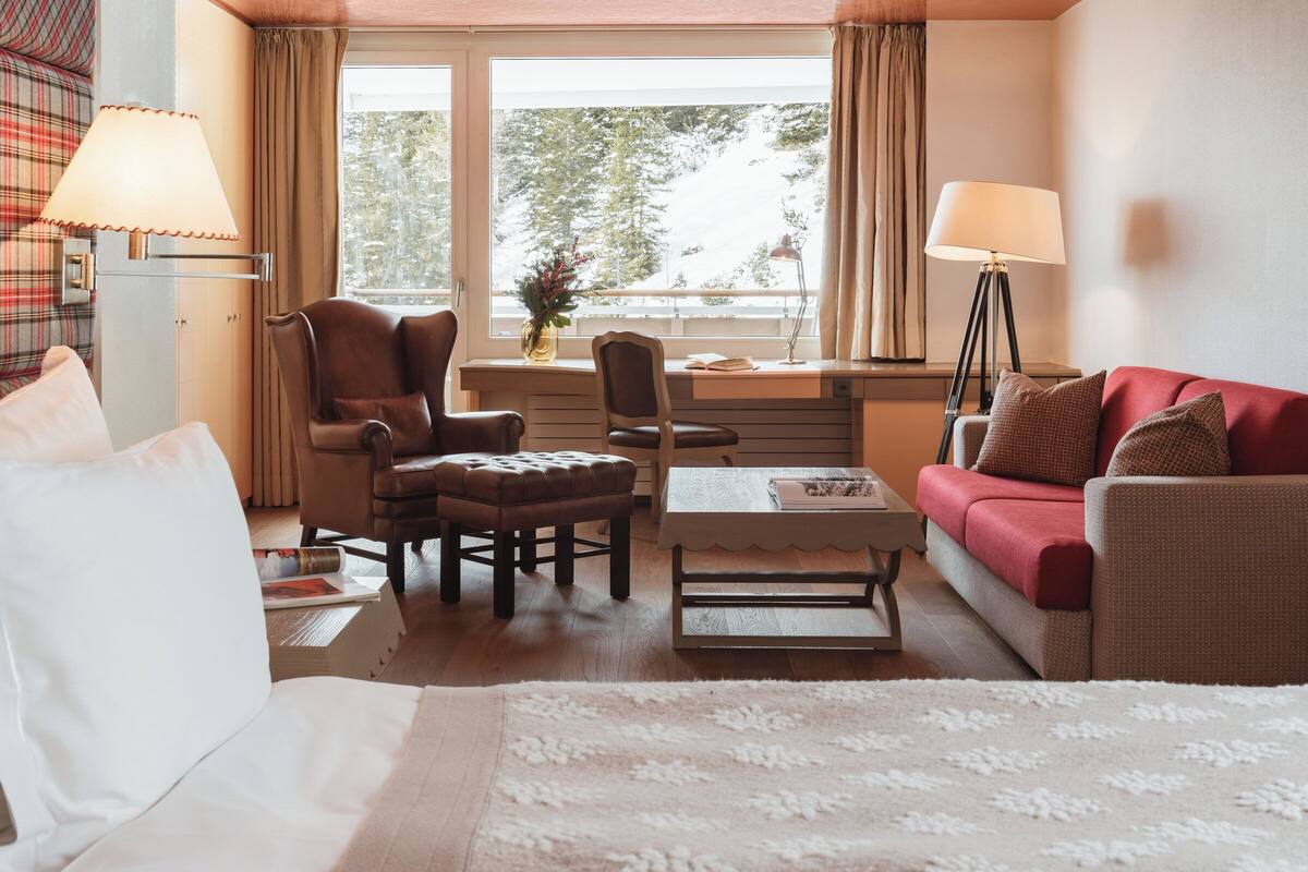 A hotel room with a bed, two armchairs, a sofa, a desk, and a window with curtains.