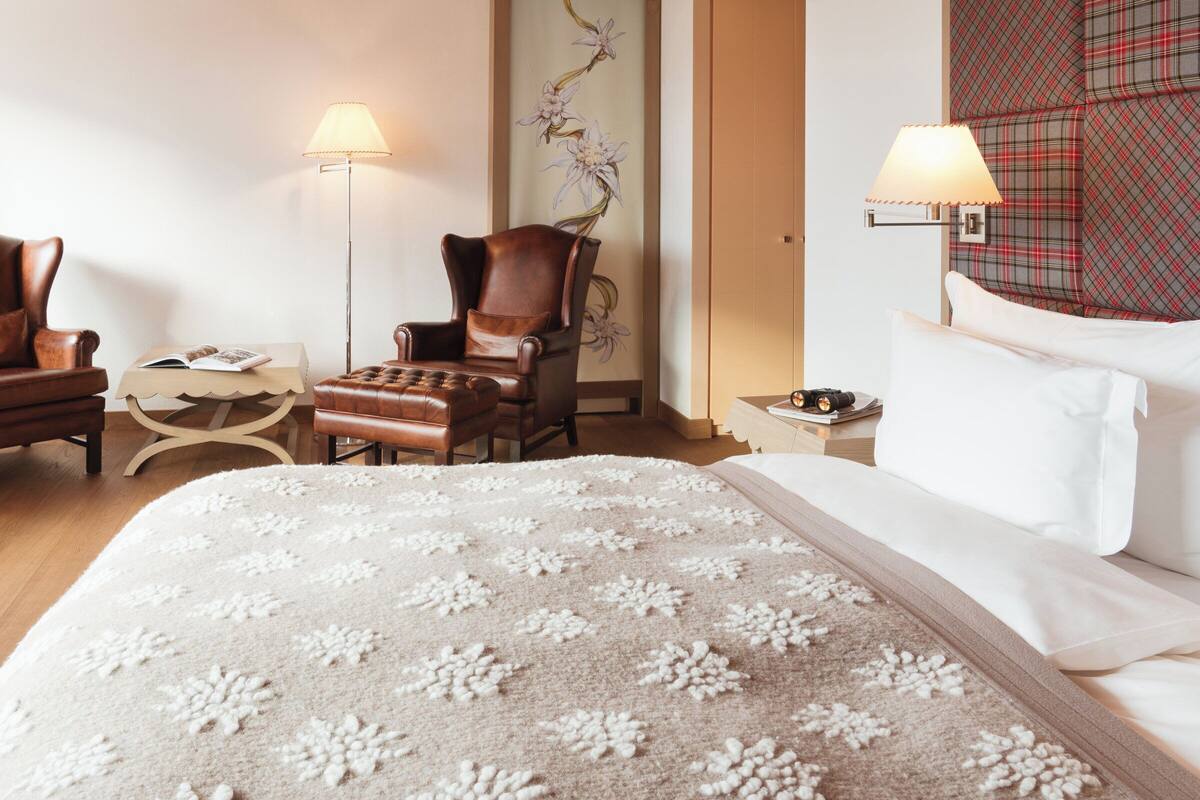 A hotel room with a large bed, a chair, a small table, a lamp, and a wall with a floral design.