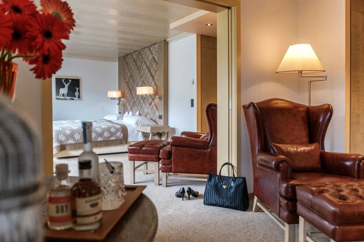 A hotel room with a bed, two armchairs, a standing lamp, and a mirror reflecting the room.